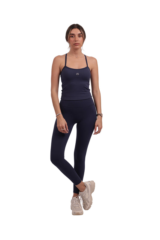 Woman wearing a navy tank top and leggings on a white background